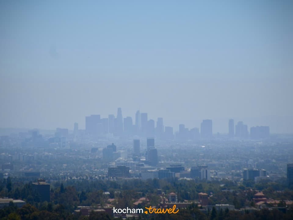 Panoramiczny widok na zamgloną panoramę Los Angeles, zielone wzgórza, jasny dzień.