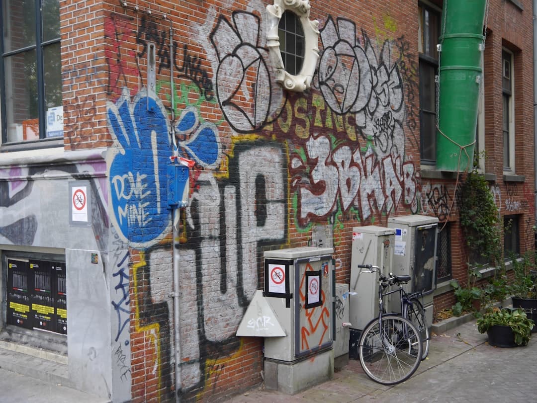 Kolorowe graffiti na ceglanym murze, rower i skrzynki użytkowe.