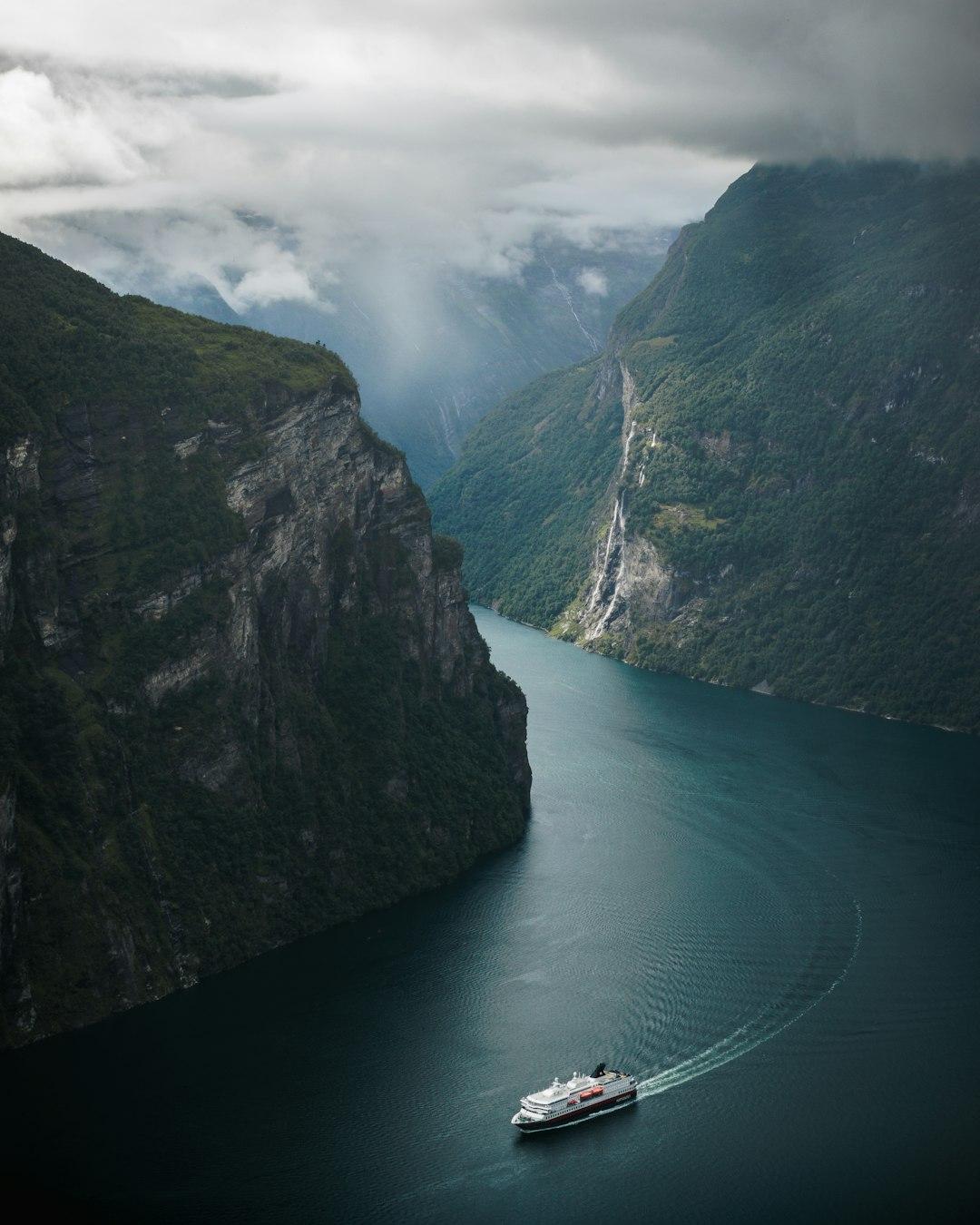 Statek wycieczkowy płynący przez norweski fiord otoczony zielonymi górami i wodospadami.