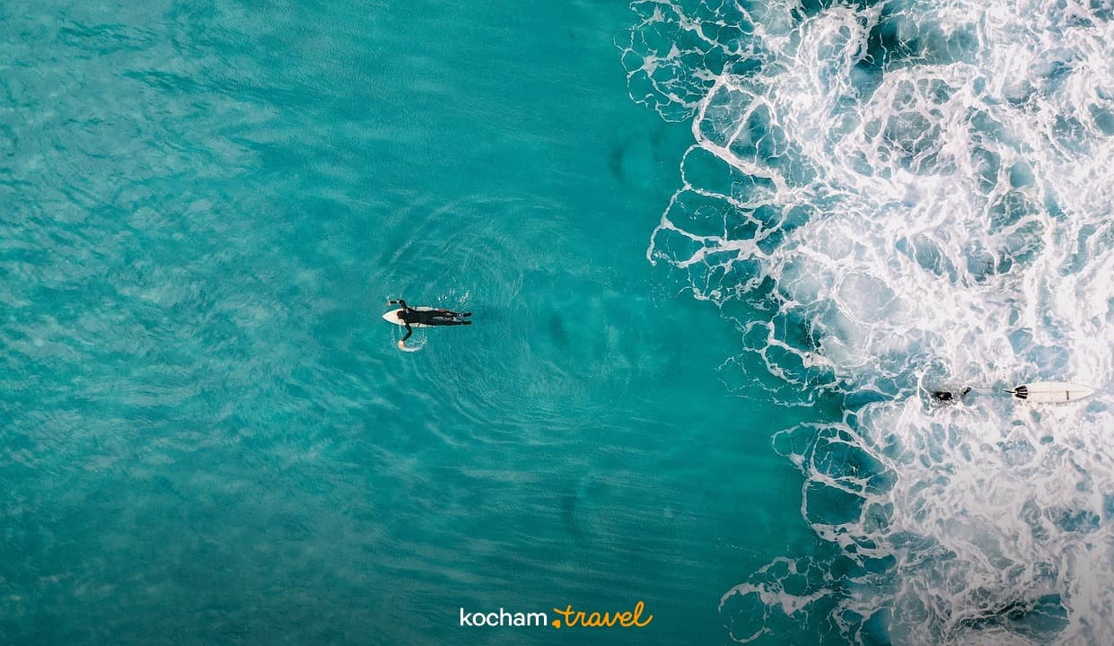 Surferzy na turkusowej wodzie oceanu z białymi falami.