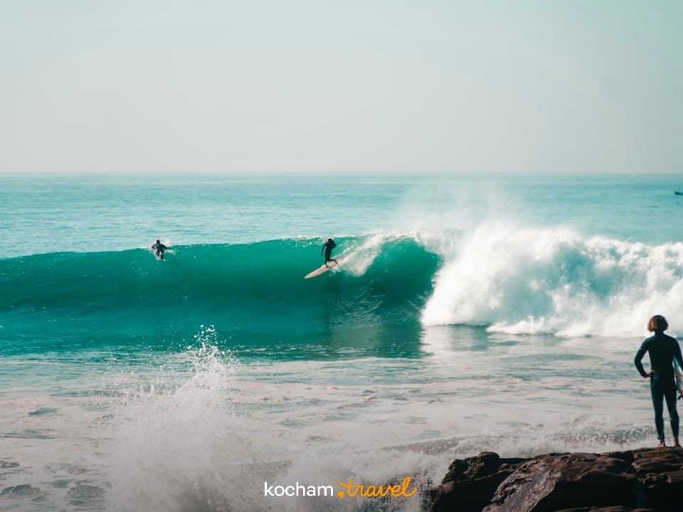 Surferzy łapiący fale na turkusowym oceanie w słoneczny dzień.
