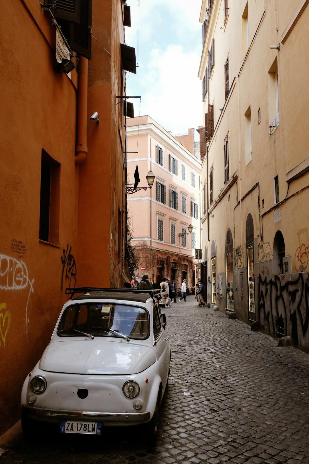 Biały zabytkowy Fiat 500 na brukowanej ulicy Rzymu z budynkami.