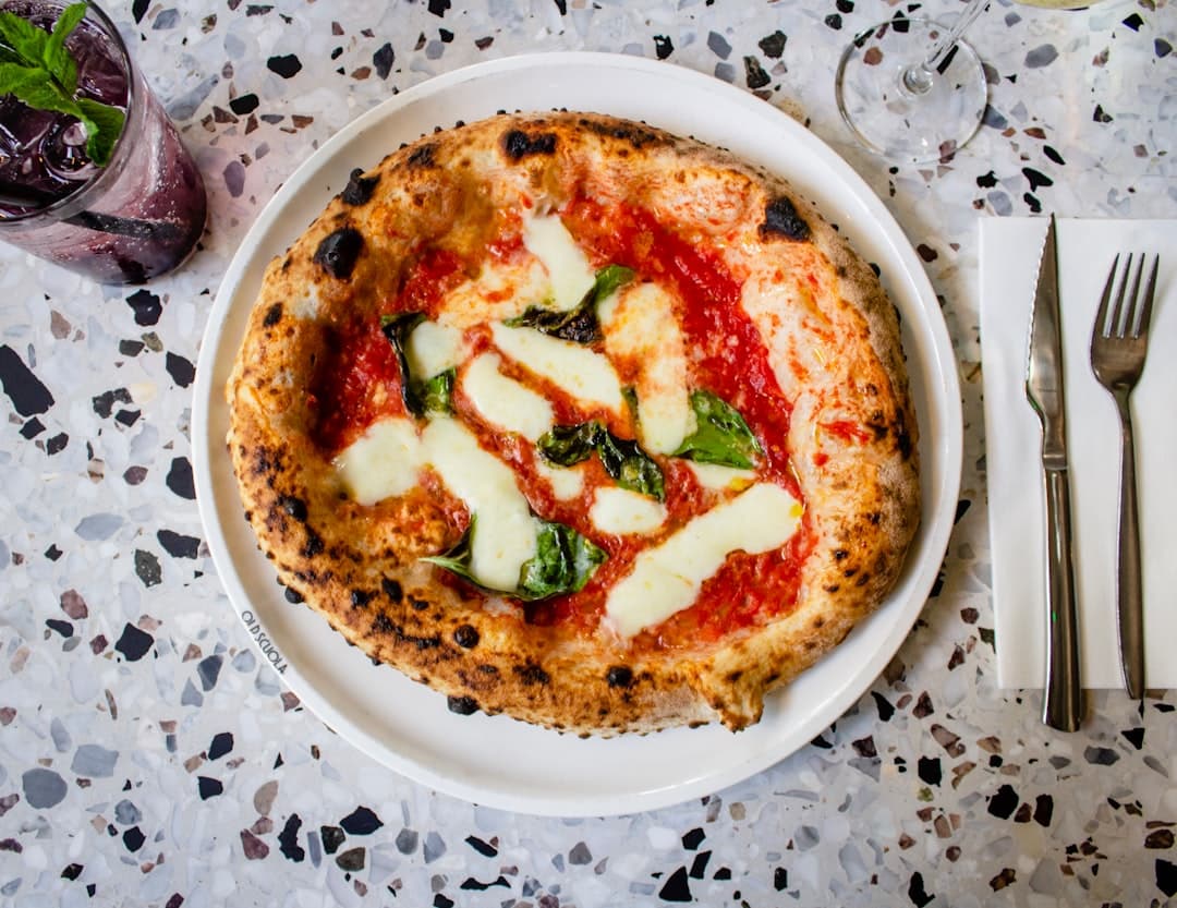 Pizza Margherita na kamiennym stole z drinkiem i sztućcami.