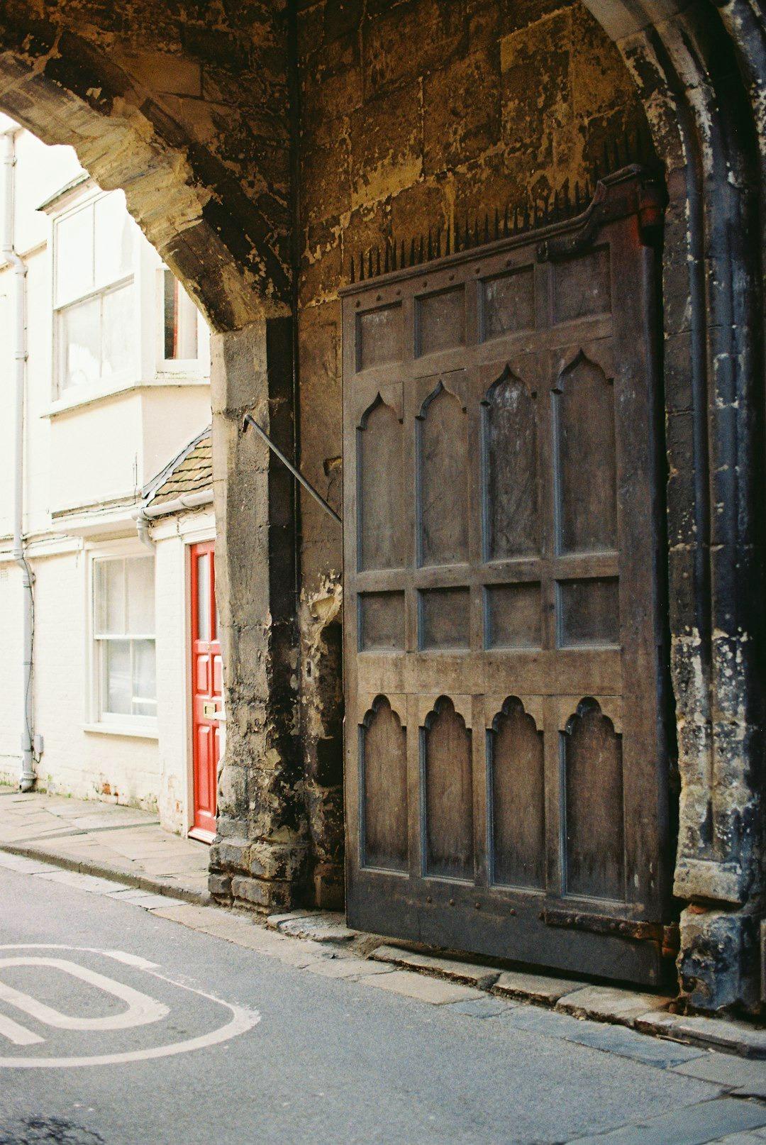 Gotyckie drewniane drzwi, kamienny łuk, historyczna europejska architektura uliczna.