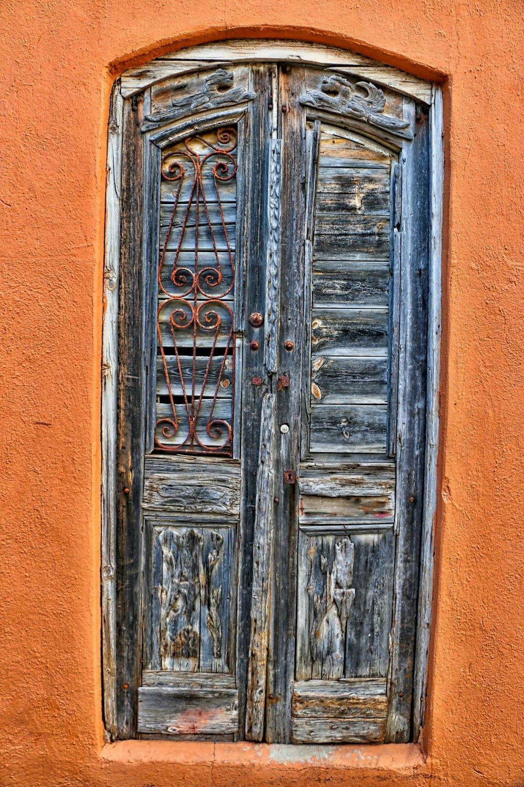 Stare drewniane drzwi, zardzewiała krata, pomarańczowa ściana, rustykalna architektura.