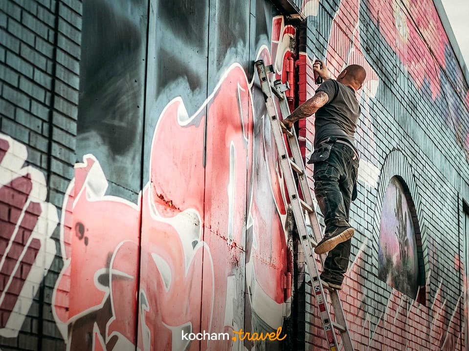Artysta graffiti malujący kolorowy mural na ceglanej ścianie.