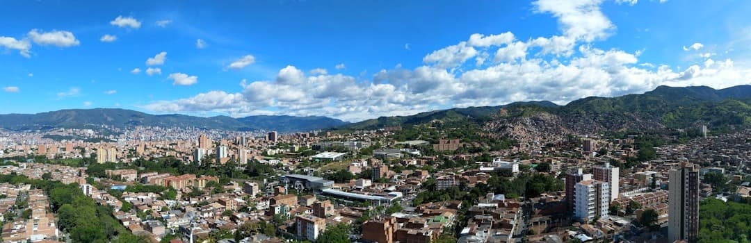 Panoramiczny widok miasta, budynki, zielone góry, błękitne niebo, jasne światło.