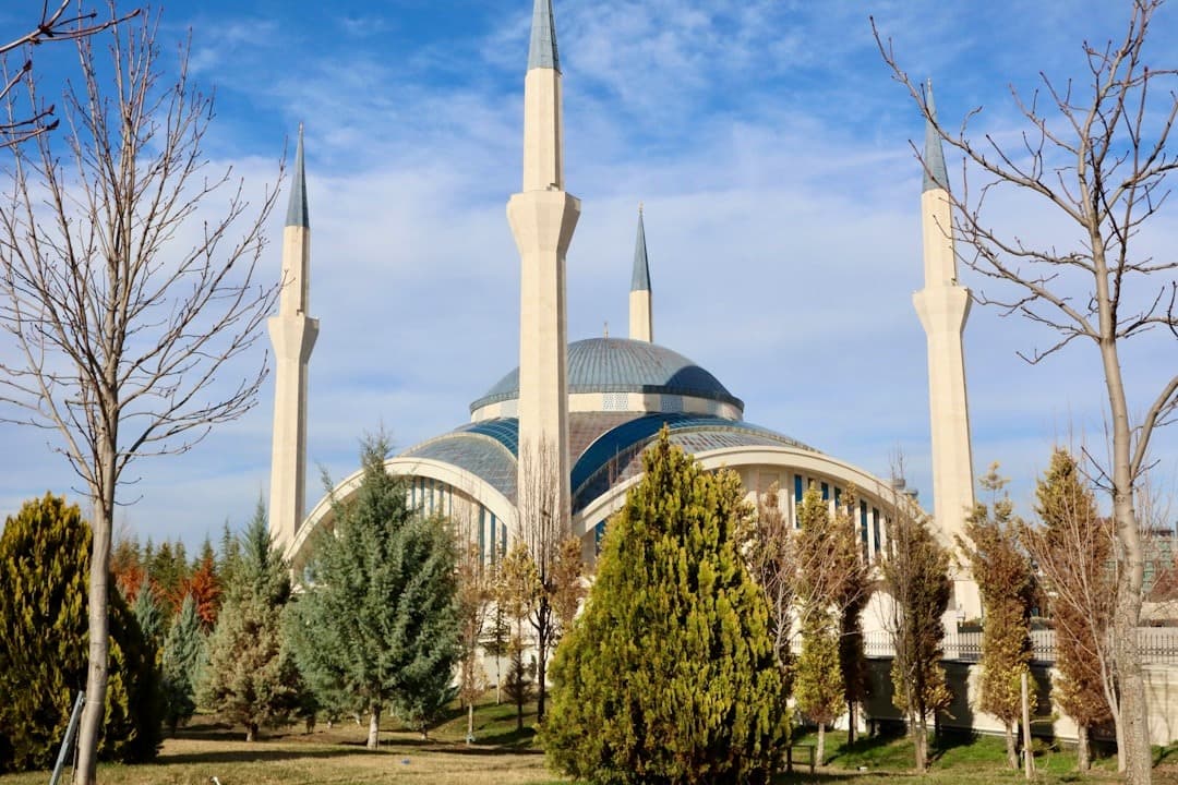 Architektura nowoczesnego meczetu z minaretami, kopułą, drzewami i błękitnym niebem.