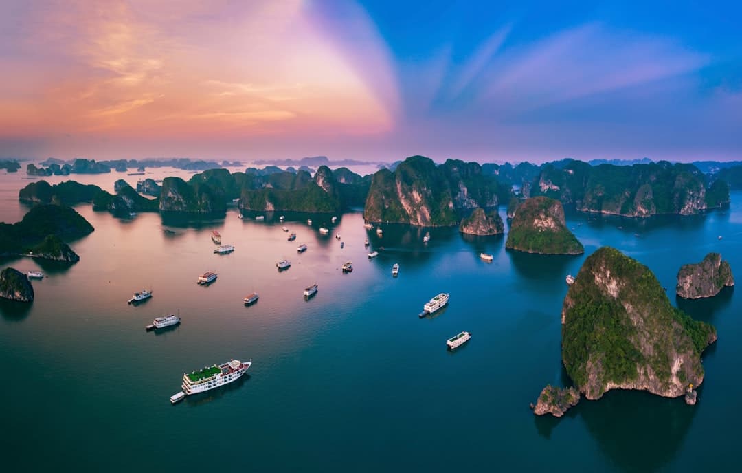Panoramiczny widok Zatoki Ha Long z wapiennymi krasami i łodziami o zachodzie słońca.