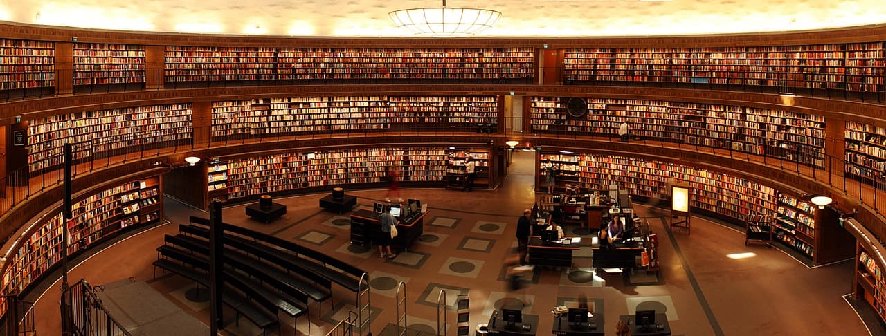 Wnętrze okrągłej biblioteki z piętrowymi półkami, książkami i czytelnikami.