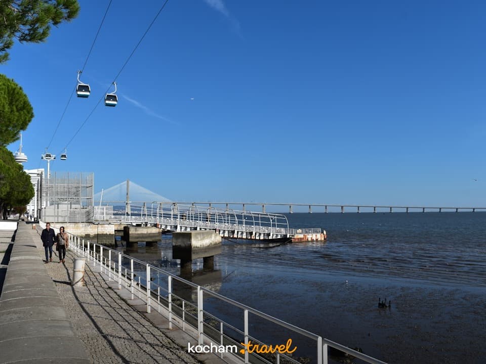 Lizbona: Promenada rzeczna, kolejka linowa, most Vasco da Gama, spacerujący ludzie.