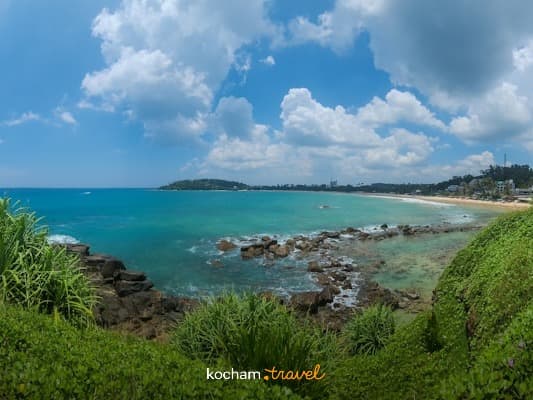 Panoramiczny widok tropikalnej plaży, turkusowa woda, zielona roślinność, błękitne niebo.