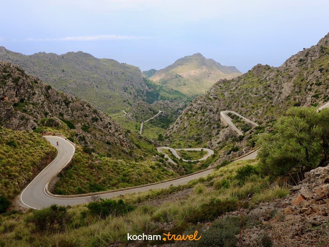 Malownicza górska droga z serpentynami, rowerzysta, skaliste wzgórza, panorama.