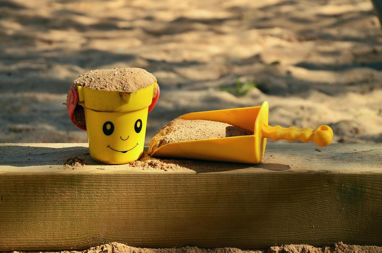 Żółte wiaderko z uśmiechem i łopatka pełne piasku na plaży.