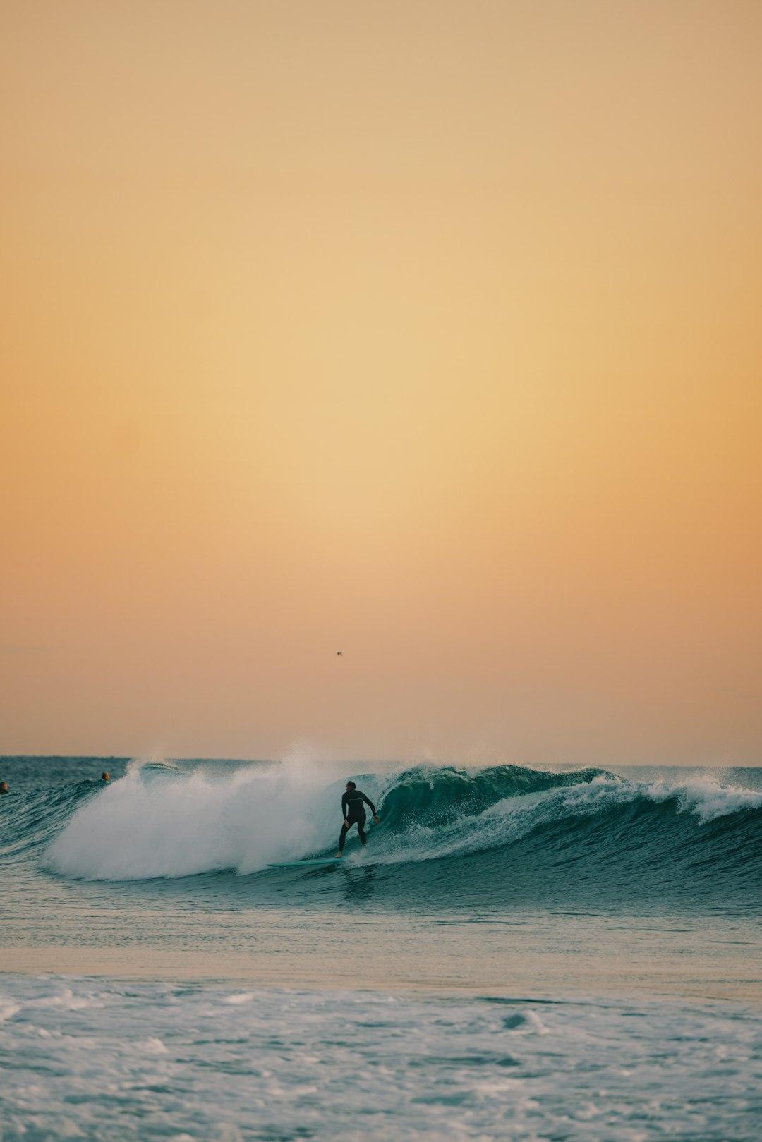 Surfer w piance łapie dużą falę na morzu o zachodzie słońca.