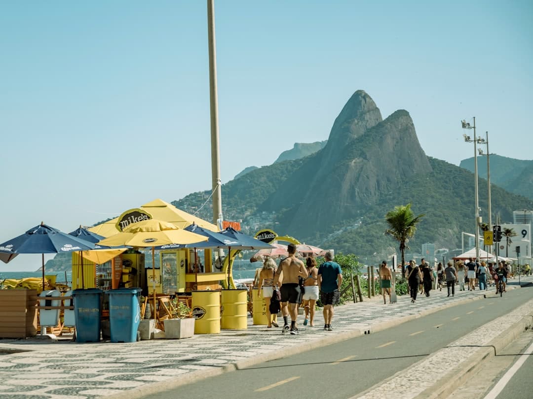 Słoneczna promenada plażowa w Rio de Janeiro z ludźmi, kioskami i górami.