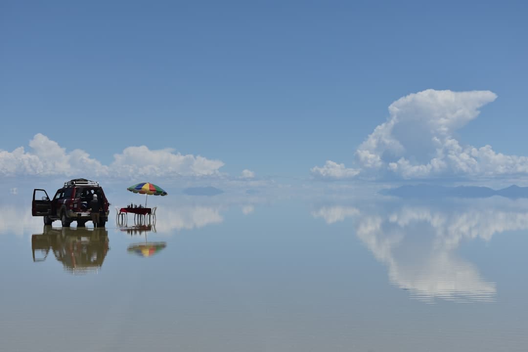 Czerwony SUV, parasol, piknik na solnisku Uyuni, odbicie nieba.