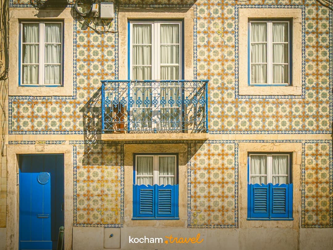 Portugalska fasada budynku, płytki azulejo, niebieskie drzwi, balkon, okiennice.