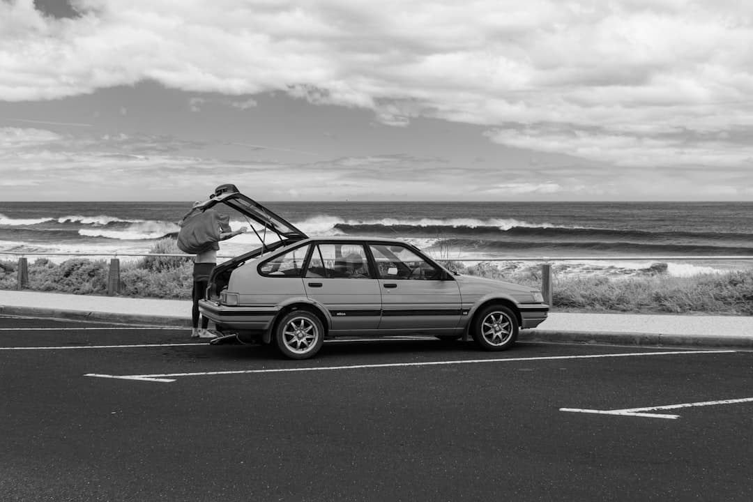 Osoba pakująca bagaż do klasycznego hatchbacka na tle wzburzonego oceanu.