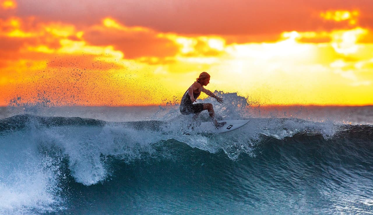Surfer na fali oceanicznej podczas pomarańczowego zachodu słońca.