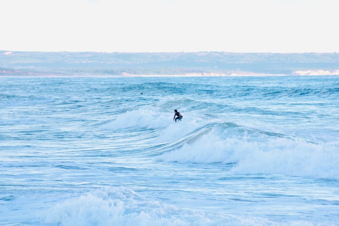 Surfer na fali oceanicznej z odległym wybrzeżem w tle.