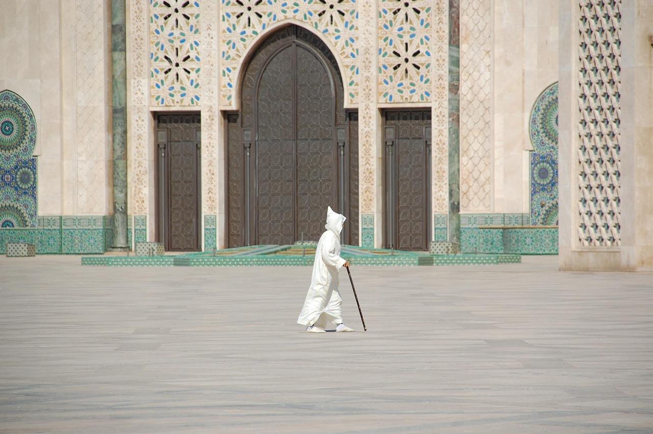 Osoba w białej szacie z laską przed meczetem Hassan II w Casablance.