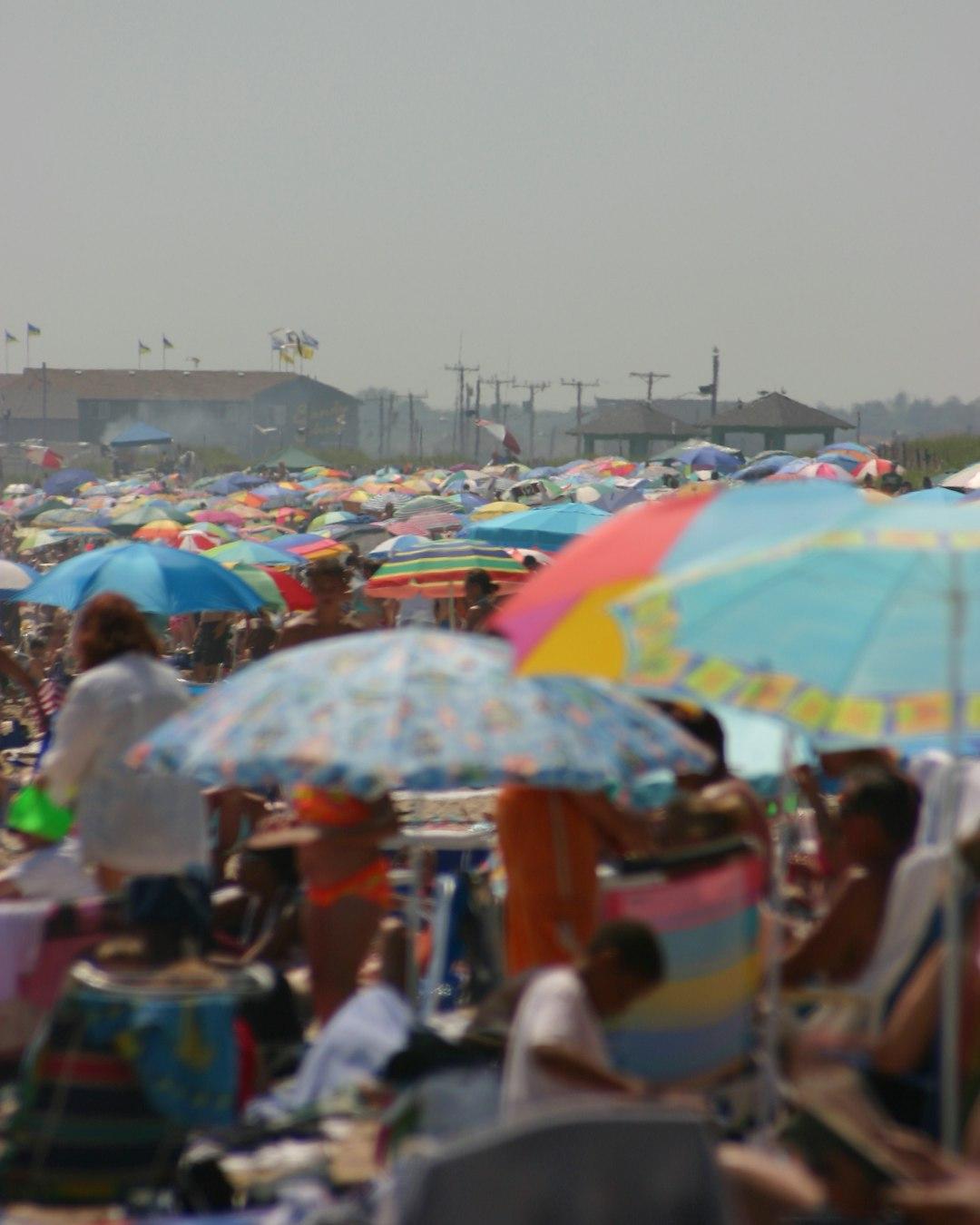 Tłum ludzi na plaży z parasolami.