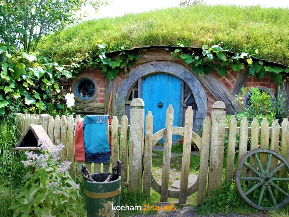 Malowniczy dom hobbita z niebieskimi drzwiami i zielonym dachem.