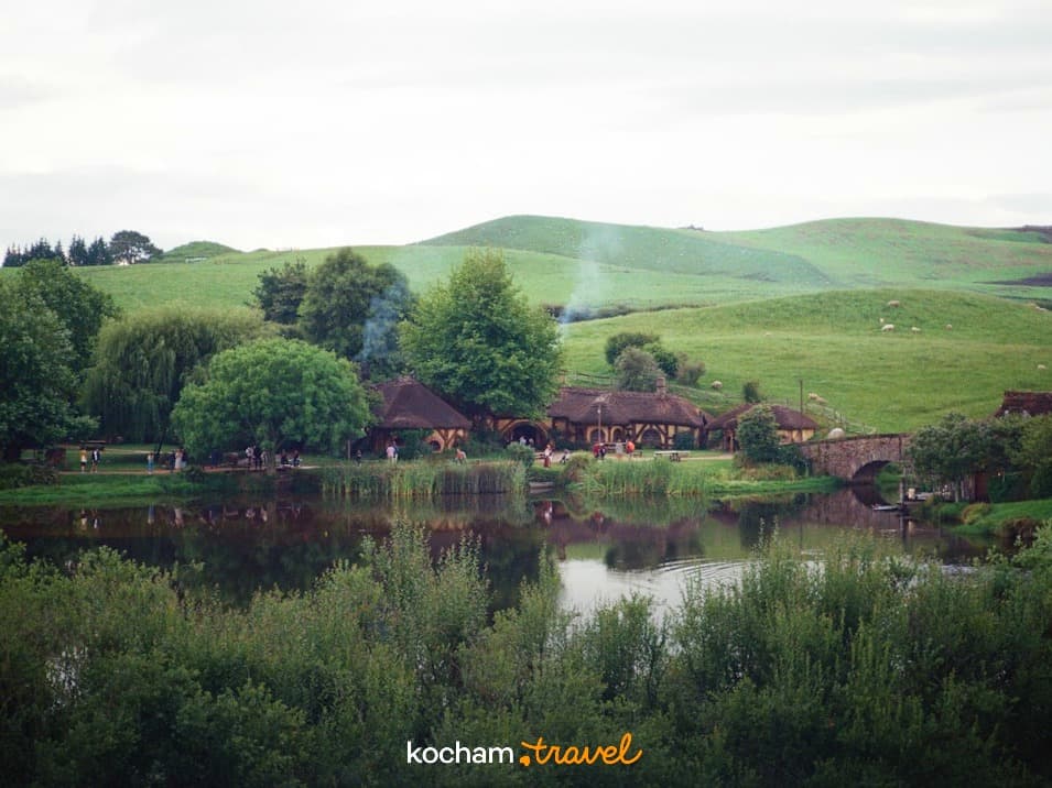 Hobbiton, Nowa Zelandia, domki hobbitów, jezioro, zielone wzgórza, most kamienny.