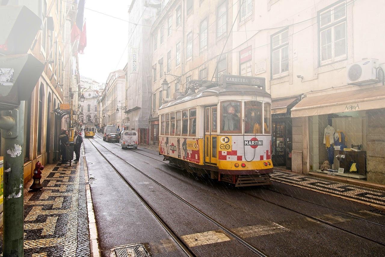 Lizbona: zabytkowy tramwaj na mokrej ulicy wśród starych kamienic.