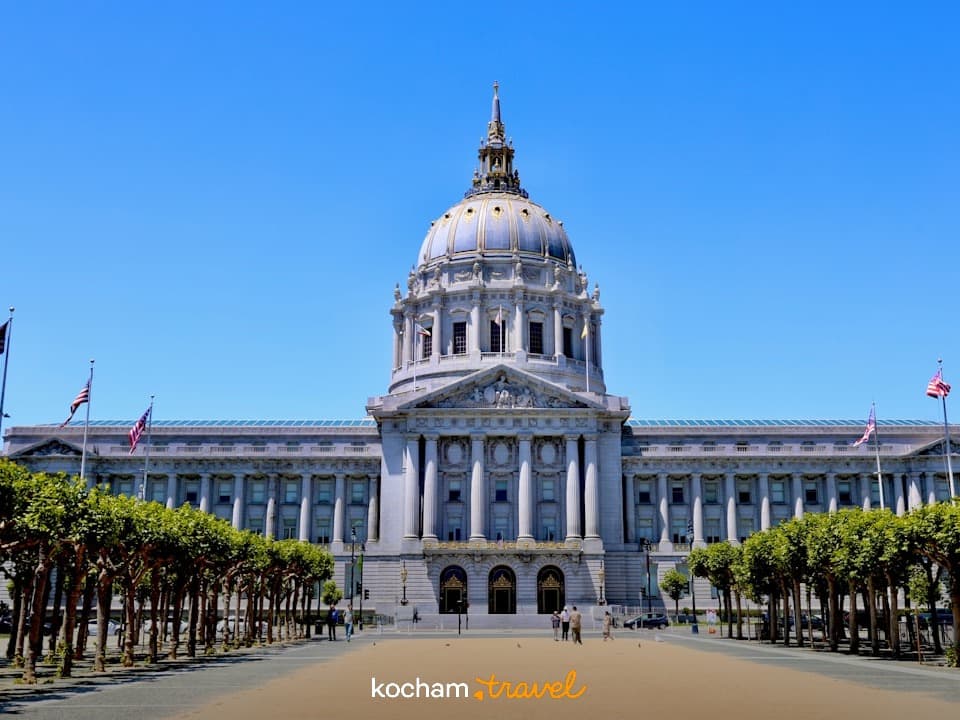 Majestatyczny Ratusz San Francisco, klasyczna architektura, kopuła, błękitne niebo, flagi, drzewa.