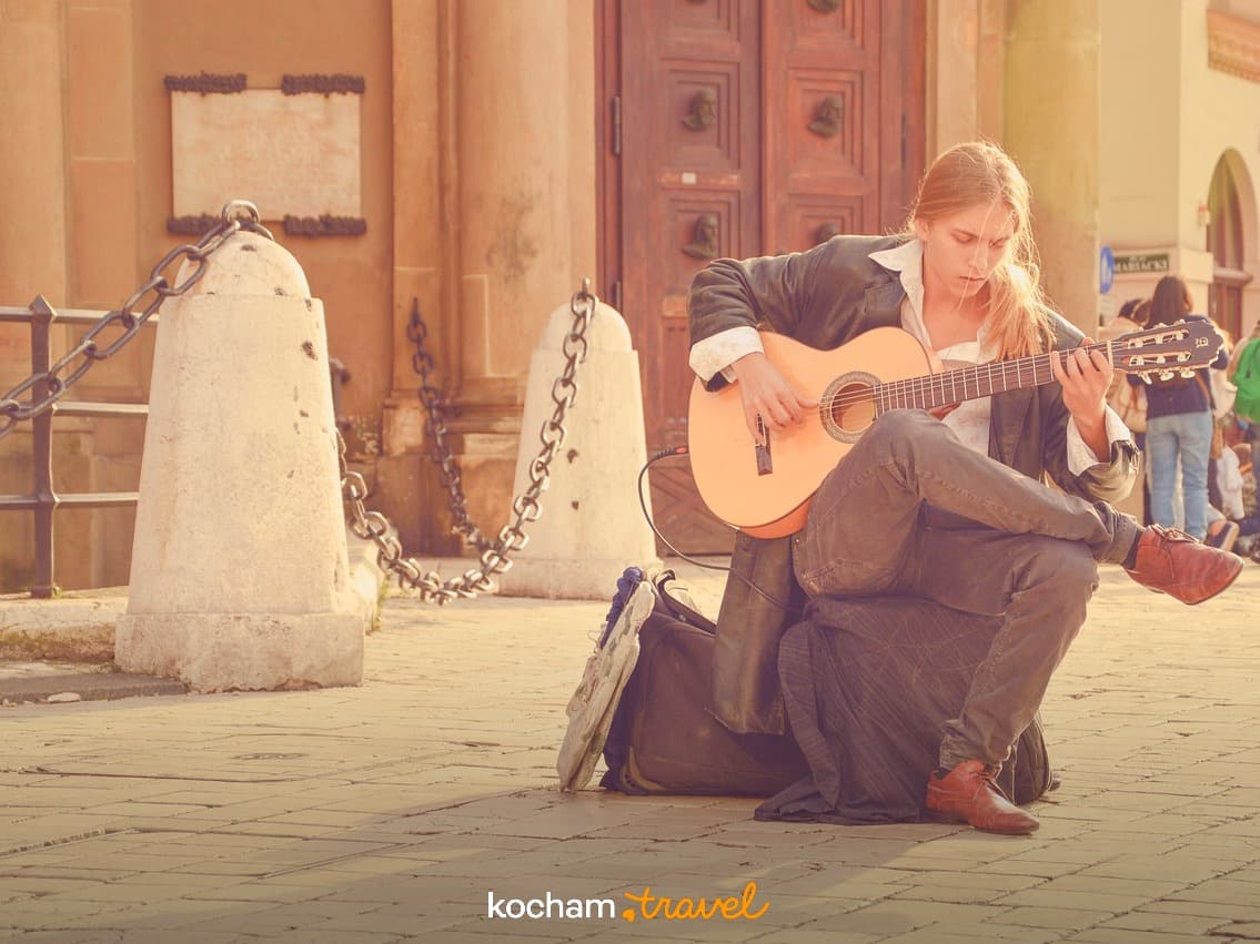 Grający na gitarze muzyk uliczny na tle zabytkowej architektury.