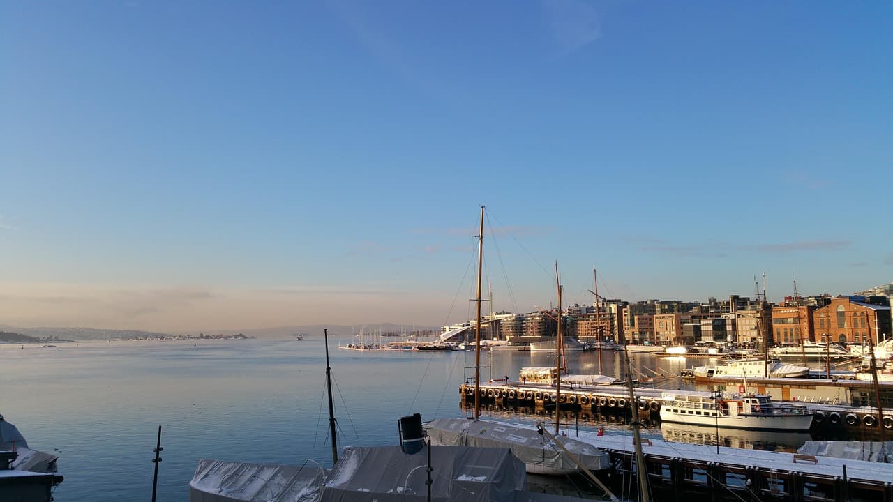 Zimowy port z zacumowanymi jachtami, ośnieżonym nabrzeżem i miejską zabudową.