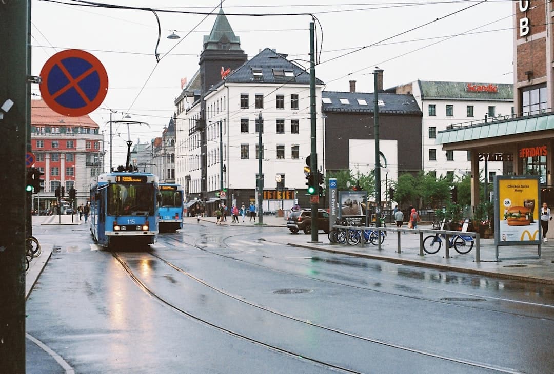 Niebieskie tramwaje na mokrej ulicy w Oslo, budynki, ludzie, rowery.
