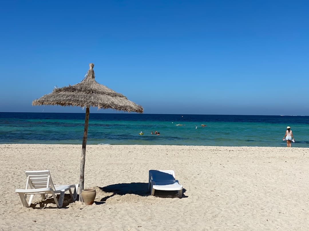 Piaszczysta plaża, parasol, leżaki, turkusowe morze i kąpiący się ludzie.