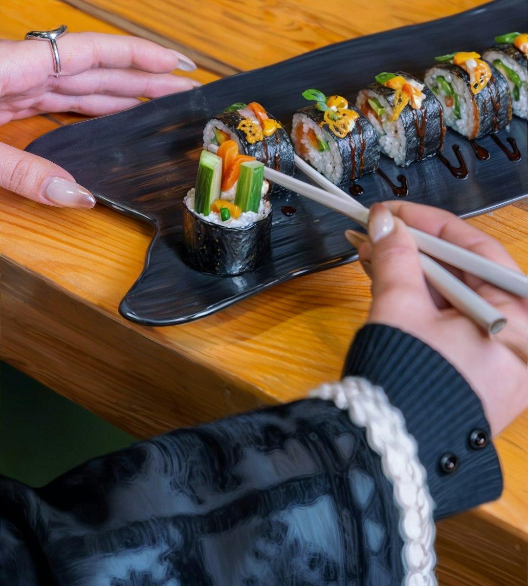 Osoba wybierająca pałeczkami kawałek sushi z eleganckiej tacy.