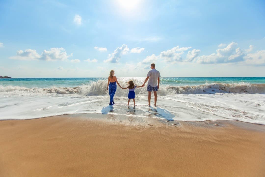 Rodzina na plaży, trzymająca się za ręce, fale oceanu, słoneczny dzień.