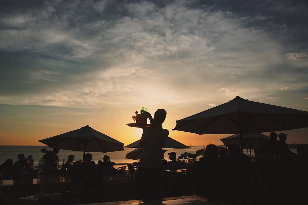 Kelner niosący tackę z drinkami na plaży o zachodzie słońca wśród gości.