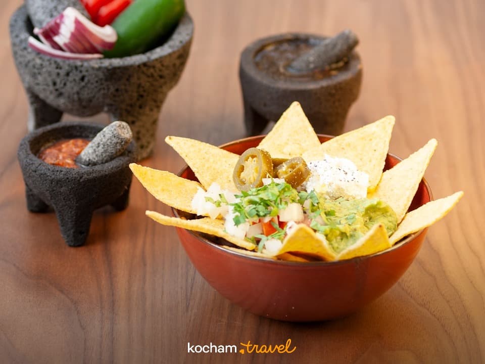 Nachos z guacamole, salsą i jalapeño, obok moździerze na drewnianym stole.