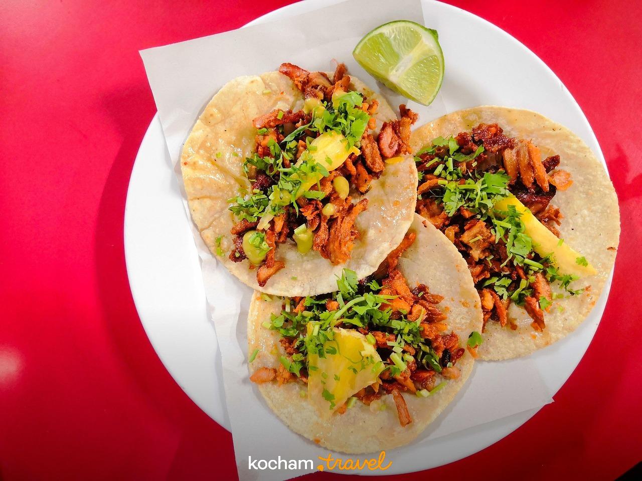 Meksykańskie tacos al pastor z ananasem i limonką na talerzu.
