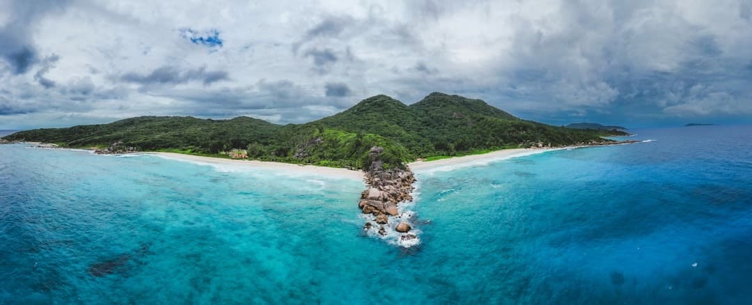 Panoramiczny widok tropikalnej plaży, turkusowa woda, zielone wzgórza.