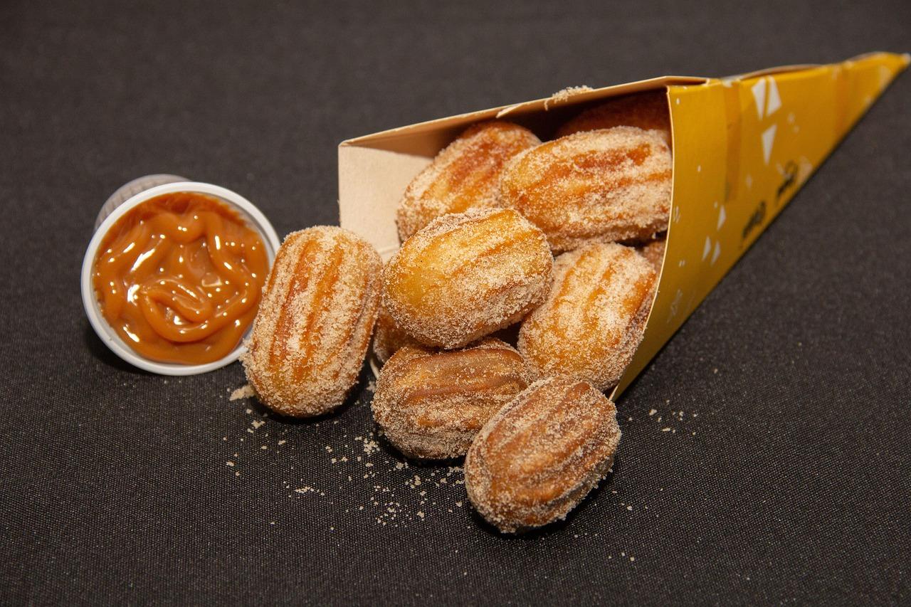 Mini churros posypane cukrem z sosem karmelowym w kubku.