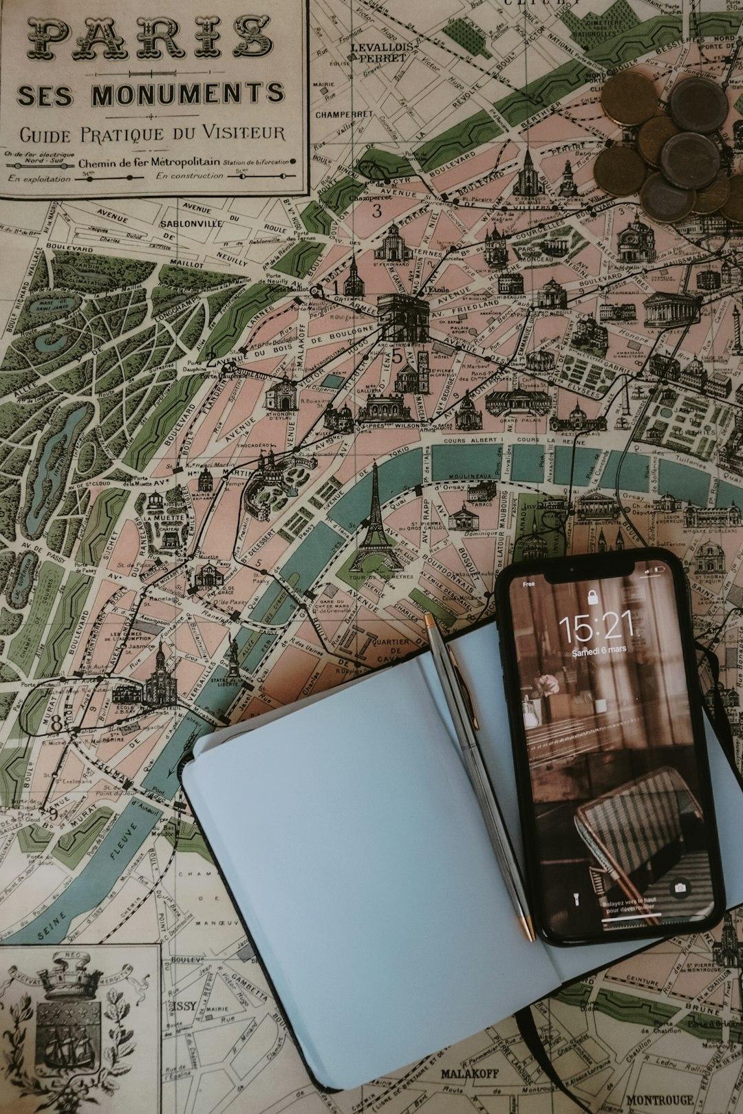 Stara mapa Paryża, smartfon, notatnik, długopis i monety do planowania podróży.