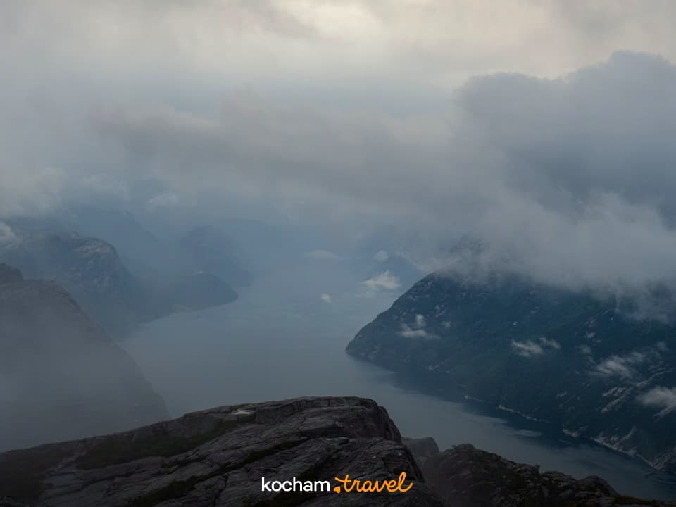 Majestatyczny fiord wśród skalistych gór pod zachmurzonym niebem.