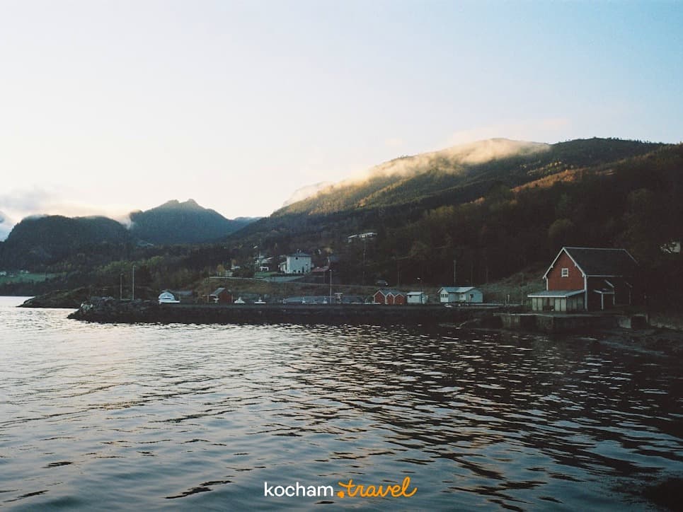 Norweska wioska nad fiordem, mgliste góry, czerwony dom, spokojna woda.
