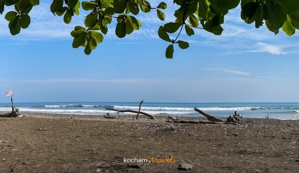 Słoneczna, panoramiczna plaża z ciemnym piaskiem, oceanem i flagą Kostaryki.