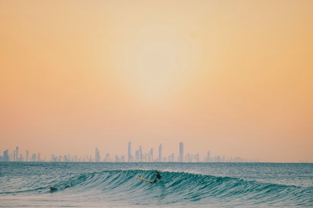 Surfer na fali z panoramą miasta w tle o zachodzie słońca