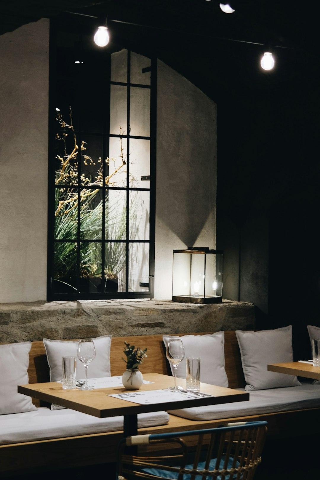 Wnętrze restauracji ze stołem, ławkami, oknem z zielenią i nastrojowym oświetleniem.