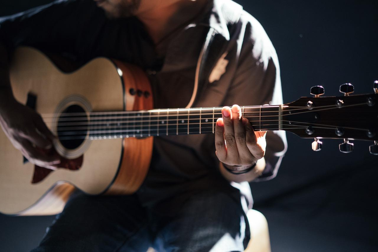 Osoba gra na gitarze akustycznej, zbliżenie na dłonie i struny.