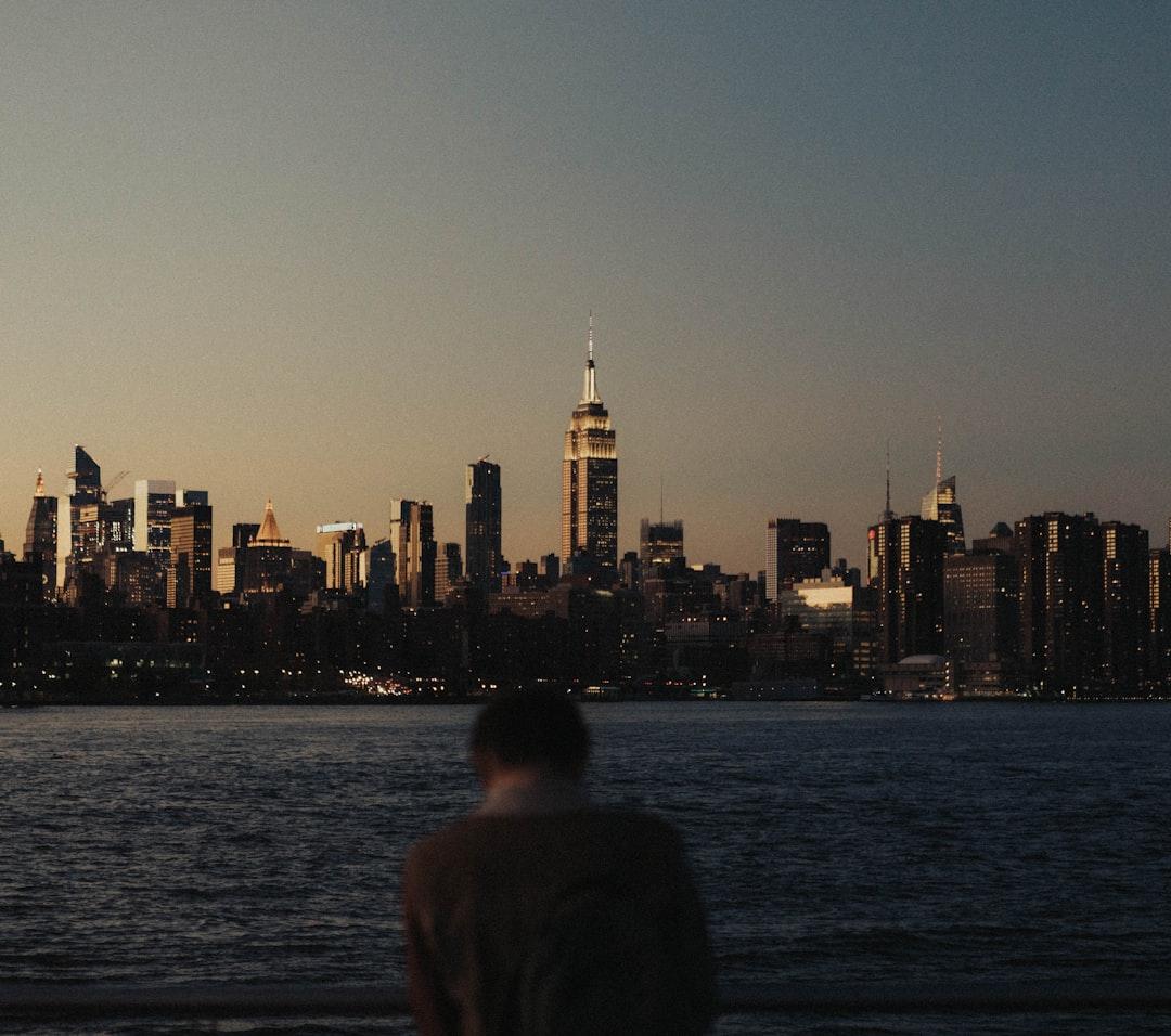 Osoba podziwiająca oświetloną panoramę Nowego Jorku i Empire State Building o zmierzchu.